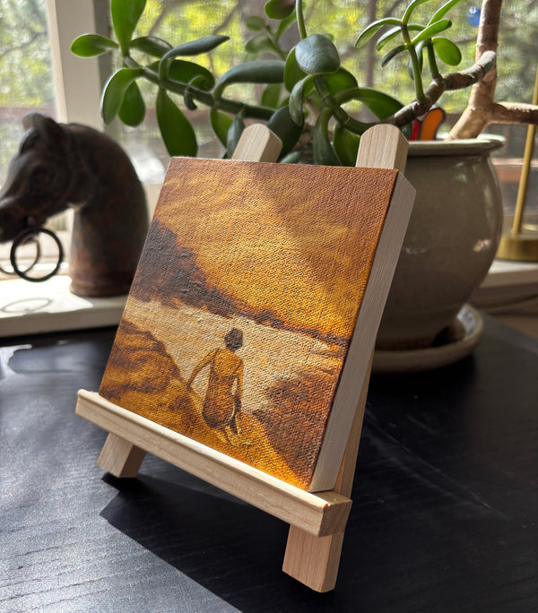 A small oil on canvas painting depicting a figure sitting on a beach in warm brown and sepia tones.
