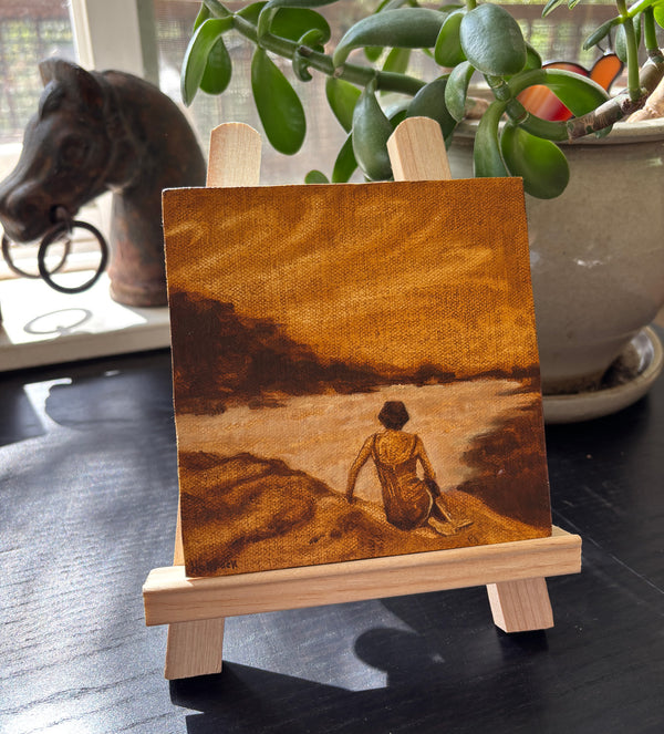 A small oil on canvas painting depicting a figure sitting on a beach in warm brown and sepia tones.
